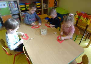 Dzieci siedzą przy stoliku, układają uśmiech z wykorzystaniem szablonu ust i ziaren fasoli.